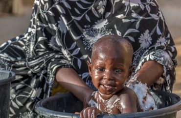 Jumai Alhassan, a resident of the Madinatu camp for Internally Displaced Persons, uses water from a solar-powered borehole water supply system funded by Rotary. Clean, free water allows her to bathe her children and care for her family, who experienced water scarcity in the camp before the system was installed. Maiduguri, Borno State, Nigeria. 27 April 2019.